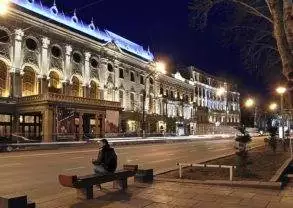 A man sits on a bench in front of a building at night in Tbilisi, Georgia.