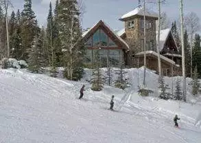 A group of people skiing down a snowy slope in front of a log cabin at Alpen Ridge Villa.