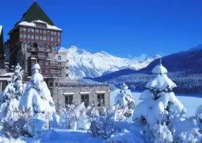 A snow covered building in front of a snow covered mountain, showcasing the grandeur of Badrutt's Palace.