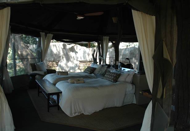 A bed in a tent with a canopy over it, surrounded by the Chongwe River Camp where elephants and hippos bathe.