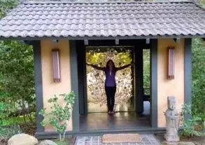 A woman standing in front of a wooden hut in the woods. Keywords: Golden Door, heaven on earth.