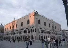 A square with many people walking around in front of an ornate building in Venice.