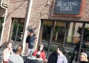 A group of people sitting at The Drafting Table outside of a restaurant.