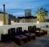Rooftop patio at dusk with chairs, tables, soft lighting, and a palm tree against city buildings, evoking the relaxed elegance of Mallorca’s Puro Oasis del Mar in Spain.