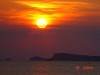 Orange sun setting over a calm sea with a dark silhouette of land below and clouds above, evoking the tranquil mood of a Chill Out evening on the coast of Spain.