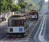 Two cable cars travel uphill on parallel tracks in San Francisco, a city lined with trees and buildings—perfect scenery for city guides and unforgettable walking tours.