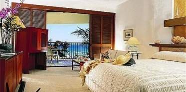 A bedroom with a balcony overlooking the majestic beauty of the Pacific Ocean at the Mauna Lani Bay Hotel and Bungalows.