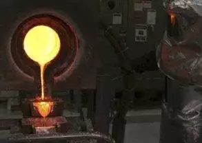 A man in a mask is pouring molten metal into a furnace at the Gold Factory.