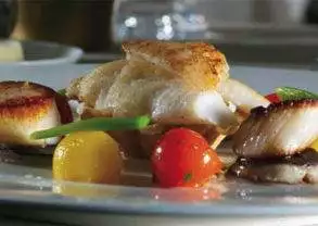 A plate with scallops and tomatoes on it at Pophams Restaurant, known for their authentic British preparations.